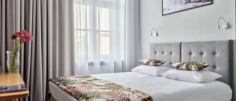A hotel room with a large bed, a bedside table with a book, a vase with flowers, and a framed picture on the wall.