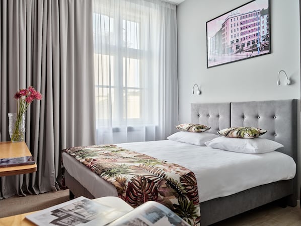 A hotel room with a large bed, a bedside table with a book, a vase with flowers, and a framed picture on the wall. - Hola Gdynia (Gdynia)