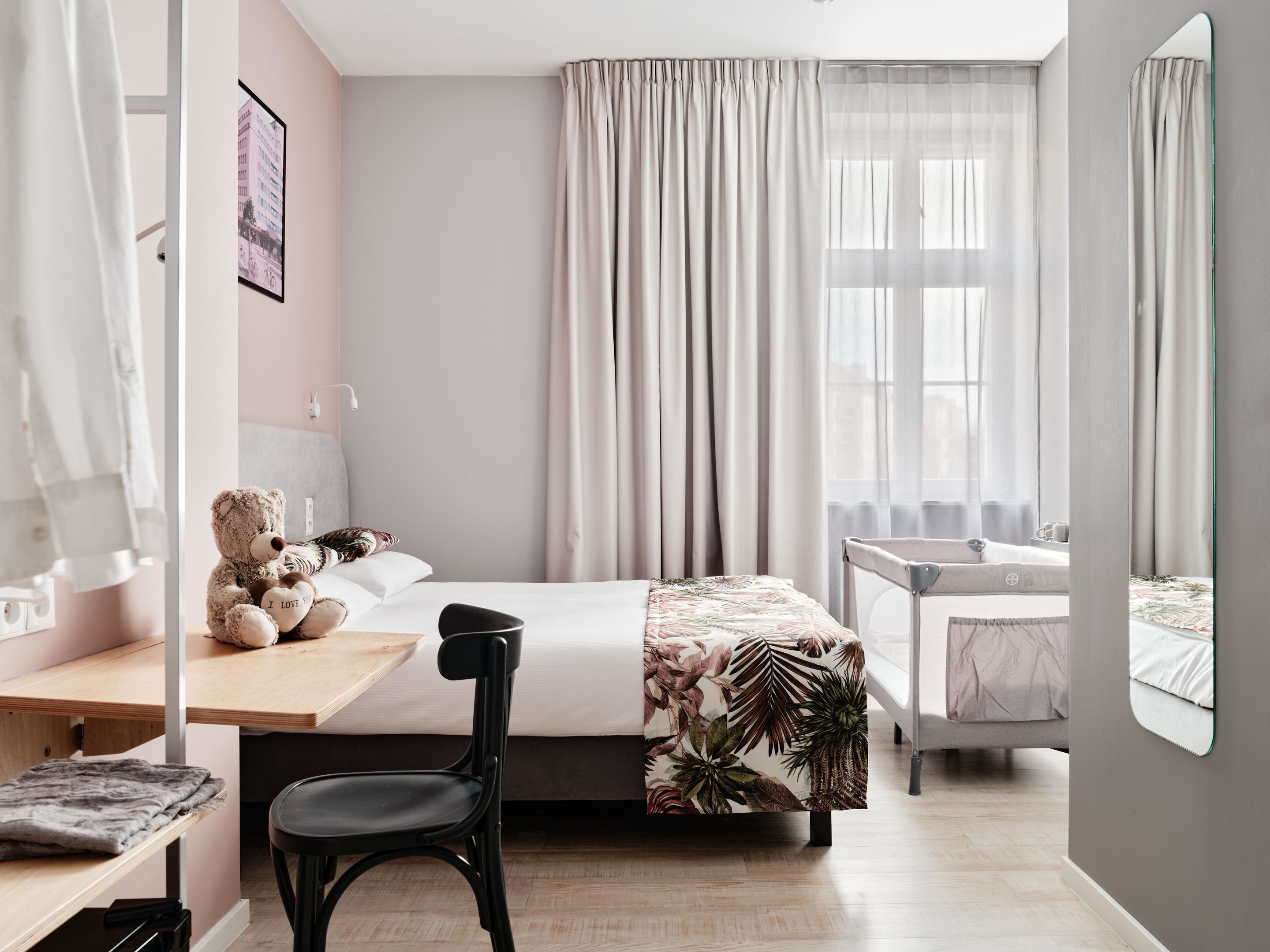 A modern bedroom with a bed, a desk, a chair, a small table, and a mirror.