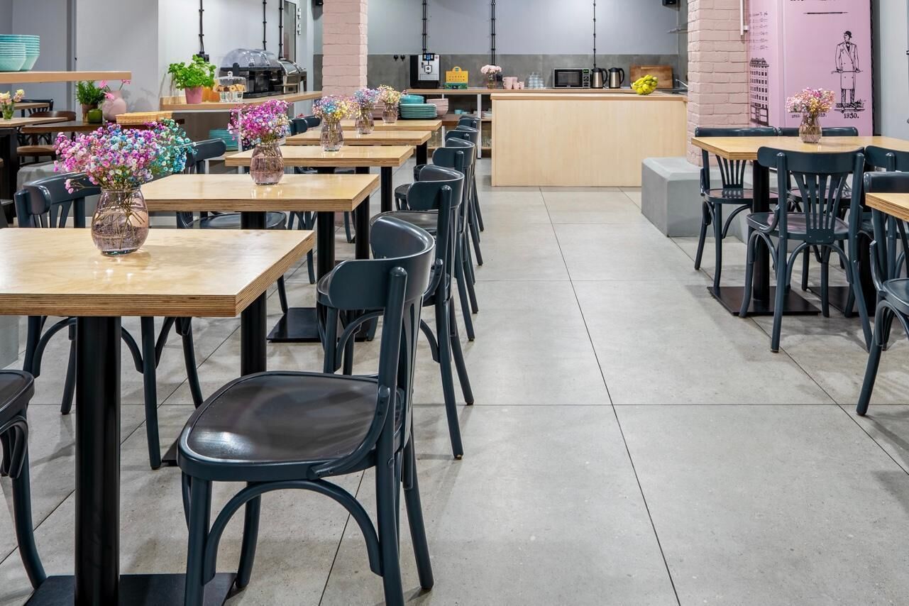 A modern dining area with multiple tables and chairs, a central counter, and decorative flowers.