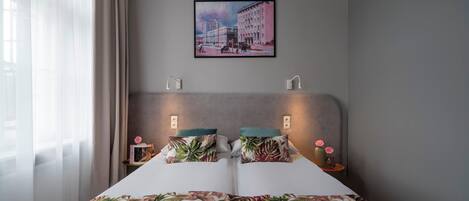 A bedroom with a bed, two bedside tables, a nightstand, a wall-mounted picture, and a window with curtains.