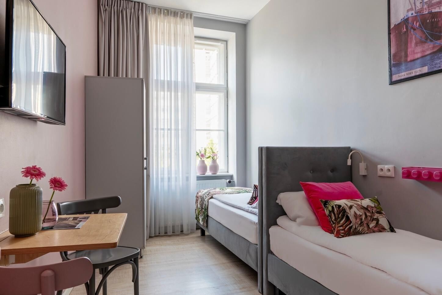 Ein kleines Hotelzimmer mit Bett, Schreibtisch, Stuhl und einem Vorhangfenster.