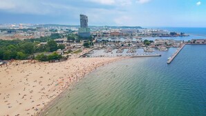 An aerial view of a coastal city with a beach, marina, and a distinctive modern building. - Hola Gdynia (Gdynia)