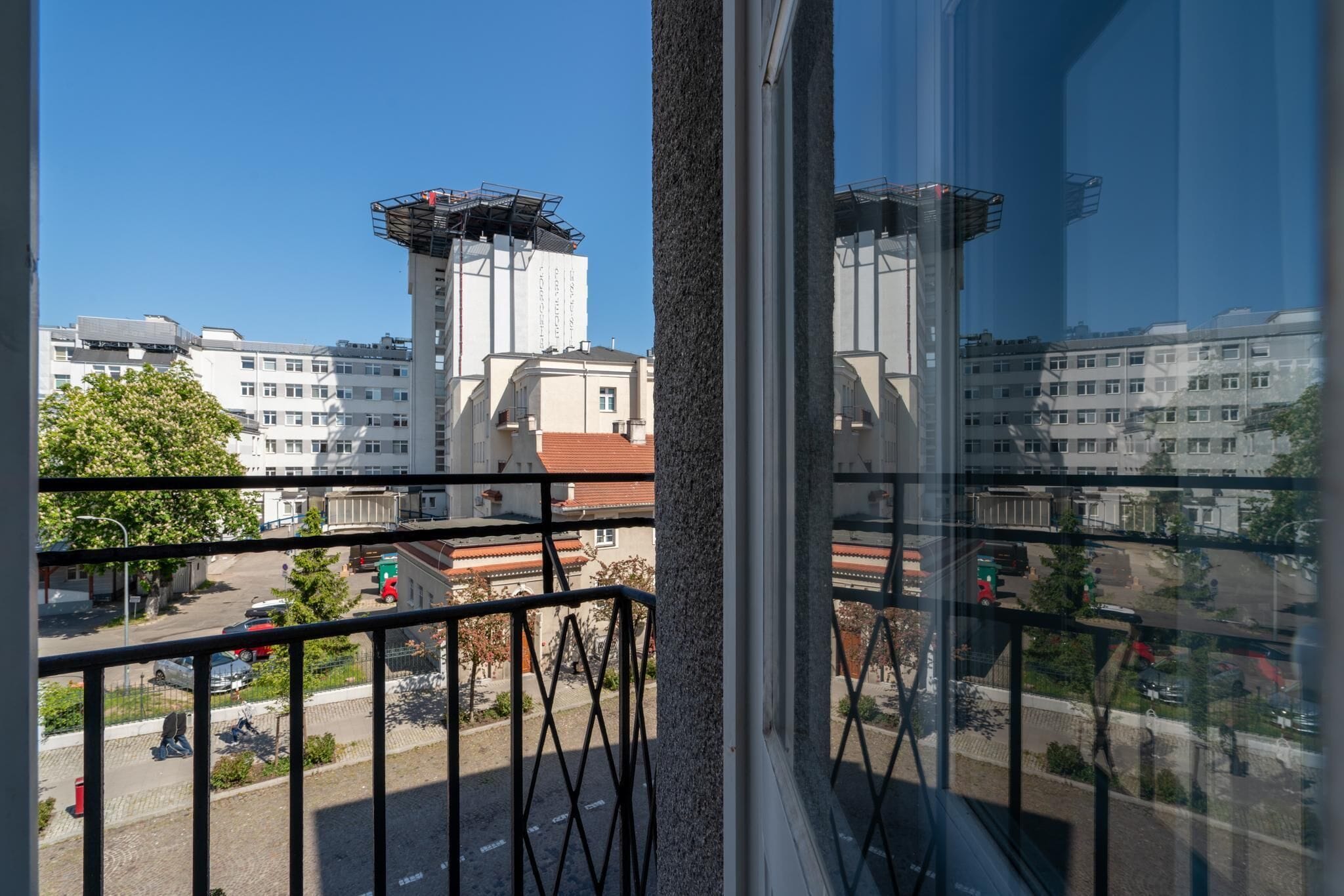 A view from a window with a metal railing, overlooking a street with parked cars and buildings in the background.