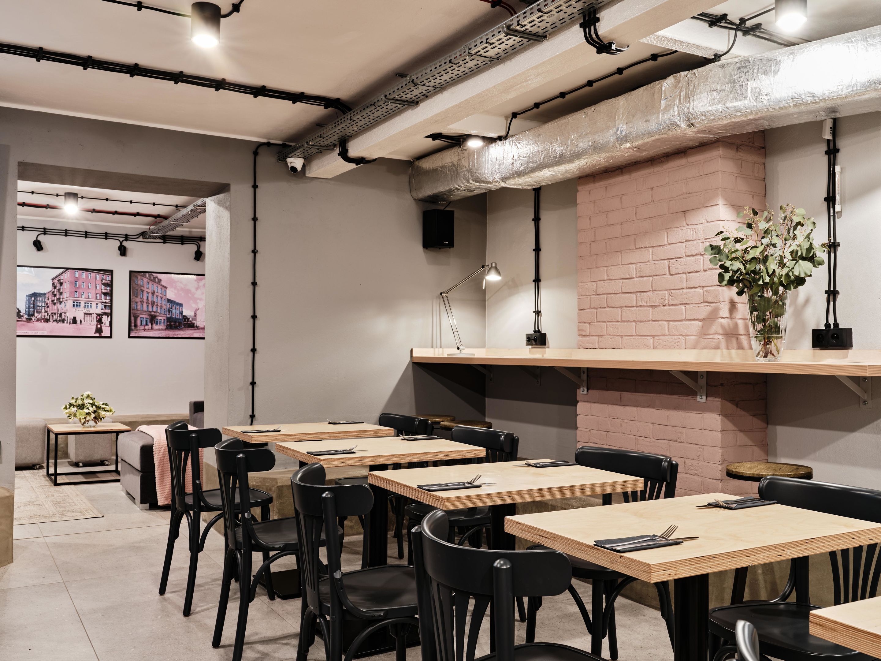 A modern cafe with wooden tables and black chairs, a brick wall, and artwork on the walls.