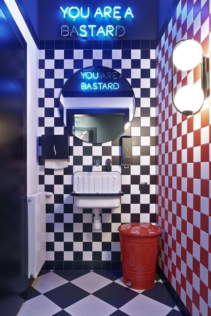 Ein Badezimmer mit Schachbrettfußboden und -wänden, einem Waschbecken, einem Spiegel und einem Mülleimer.