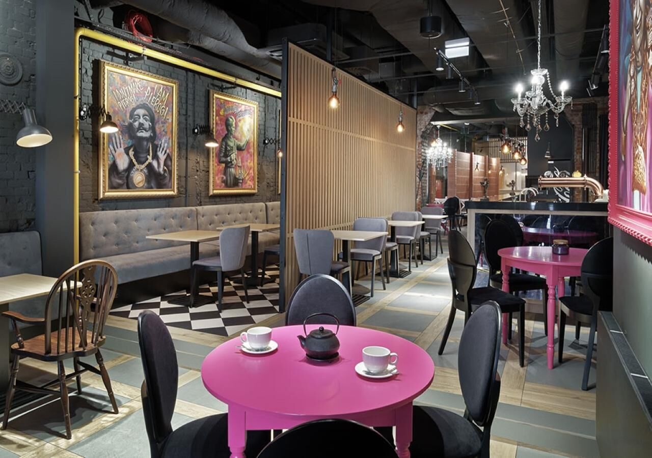 A modern cafe with round tables, some with pink tablecloths, and a mix of wooden and upholstered chairs.
