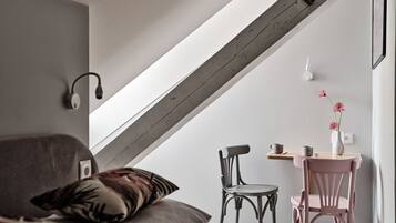 Un dormitorio estilo loft moderno con techo inclinado, cama con cojín estampado, escritorio con silla y un florero con flores.