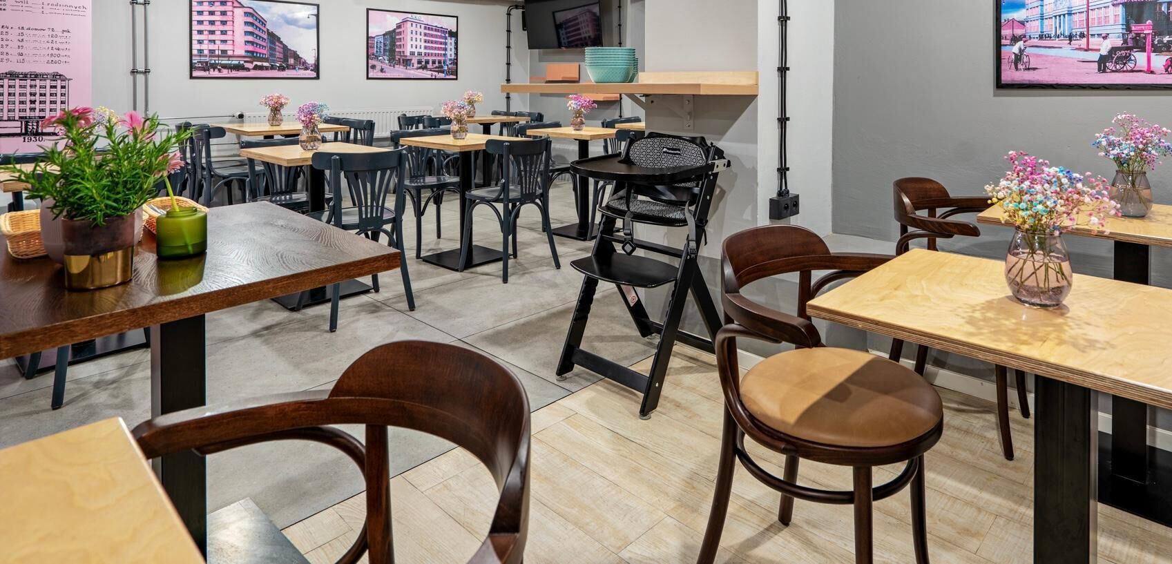 Ein Restaurant mit Holztischen und -stühlen, Blumentöpfen und gerahmten Bildern an den Wänden.