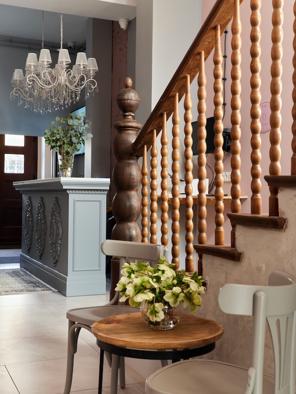 A staircase with wooden balusters, a chandelier, and a vase with flowers on a table. - Hola Gdynia (Gdynia)