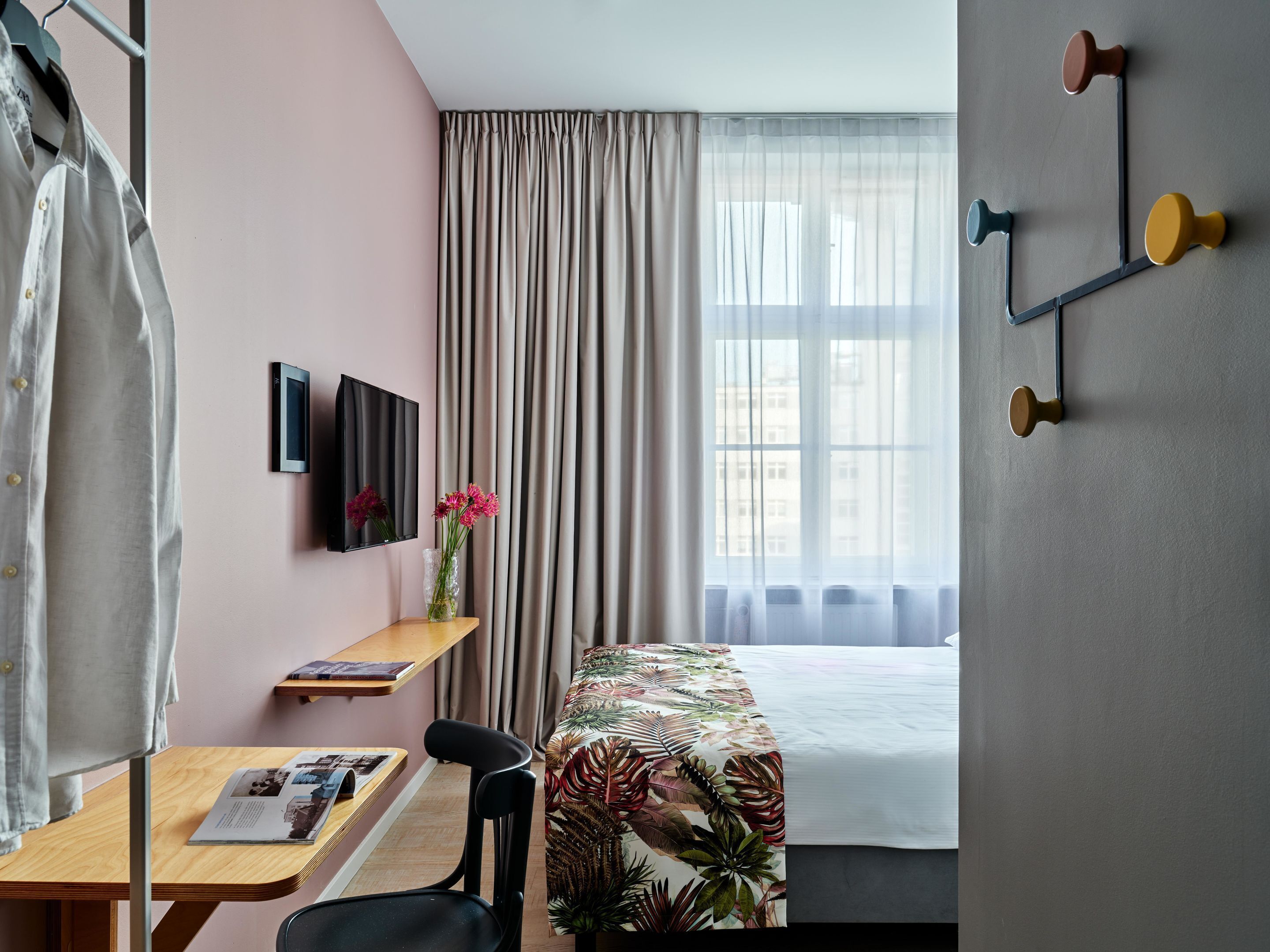 Habitación de hotel con cama, escritorio con silla, televisión en la pared y ventana con cortinas.