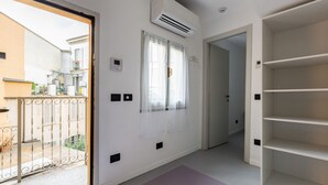 A room with a sliding glass door leading to a balcony, a white air conditioning unit, a door with a handle, and a white shelving unit. - GuestHost - APT overlooking quiet inner courtyard! (Milano)