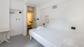 A hotel room with a bed, a small table, a bathroom visible through an open door, and a wall-mounted light fixture. - GuestHost - APT overlooking quiet inner courtyard! (Milano)
