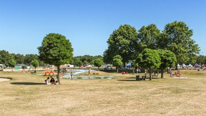 Un parco all'aperto con aree picnic, alberi e un piccolo stagno.