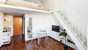 Un apartamento moderno con piso de madera, un comedor con mesa y sillas, una cocina con carrito, una escalera y una planta en maceta.