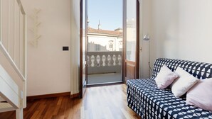 Una habitación con piso de madera, un sofá con tapicería estampada y vistas a edificios a través de una puerta de cristal.