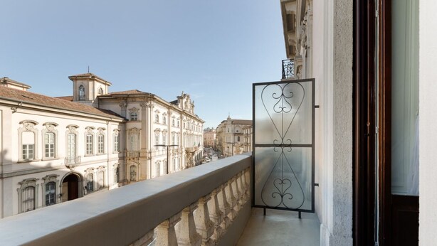 Un balcón con una reja de hierro forjado, que da a una calle con edificios históricos.