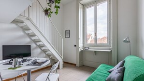 A modern room with a dining table, chairs, a green sofa, a staircase, and a window with a view of buildings.