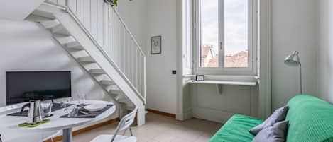 Una habitación moderna con una mesa de comedor, sillas, un sofá verde, una escalera y un ventanal con vistas a edificios.