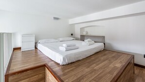 A modern bedroom with a wooden floor, a single bed with white linens, a small bedside table, and a white wardrobe.