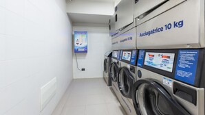 A laundry area with multiple washing machines labeled 'Asciugatricie 10 kg,' a control panel, and a 'Laundry Point' sign.