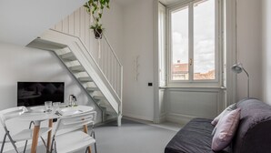 A modern living space with a staircase, a dining area, a sofa, and a window with a view.