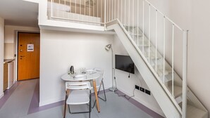 Un apartamento moderno con una escalera blanca, una pequeña mesa de comedor y un televisor montado en la pared.