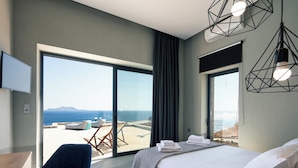 A modern hotel room with a large bed, a desk, a chair, and a balcony with a view of the sea.