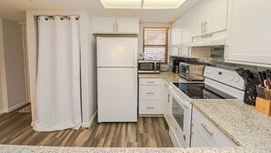 A compact kitchen with white cabinets, a refrigerator, microwave, toaster, and stove.