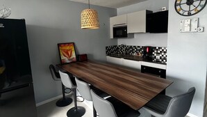 Una cocina moderna con una mesa de comedor de madera, taburetes de bar, una lámpara colgante, un microondas y un reloj de pared.