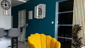 Una sala moderna con un sillón amarillo brillante, una mesa de centro de cristal y una pared de acento color turquesa.