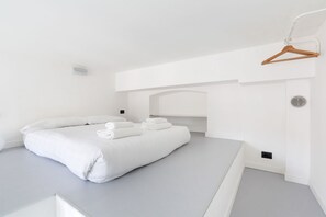 Et minimalistisk hotelværelse med en stor seng, en træbøjle og et hvidt loft.