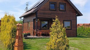 A wooden cabin with a porch, a satellite dish, and a small tree in the yard.