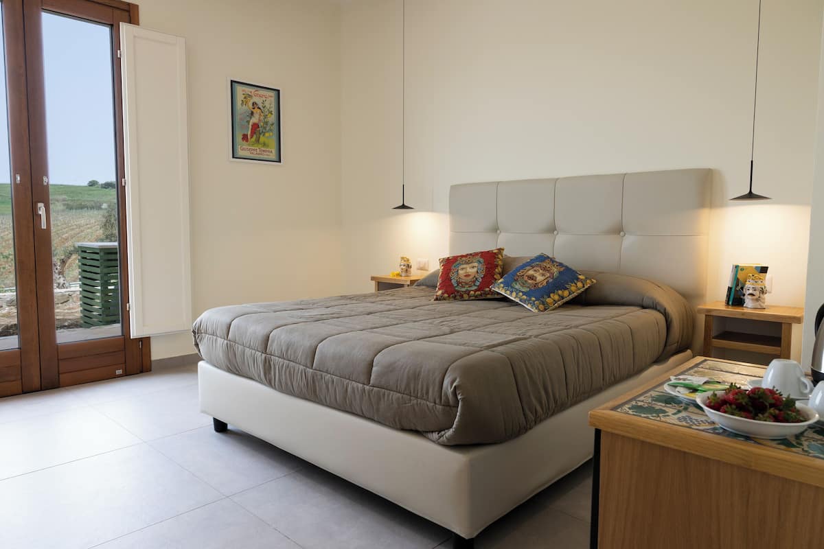 Un dormitorio con una cama, mesitas de noche, una ventana y una puerta.