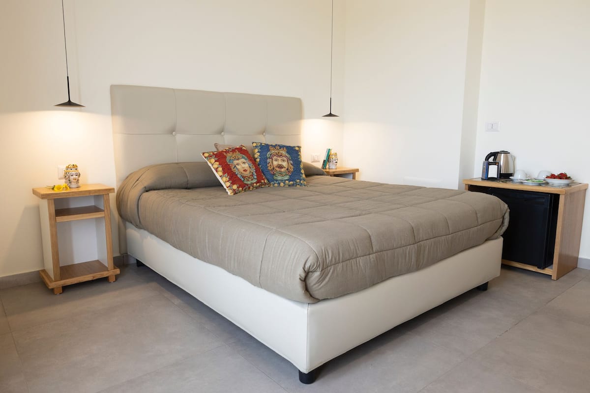 Un dormitorio ordenado con una cama grande, dos mesitas de noche y un pequeño armario.