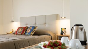 Habitación de hotel ordenada con una cama, una mesita con un frutero, tazas y una tetera.