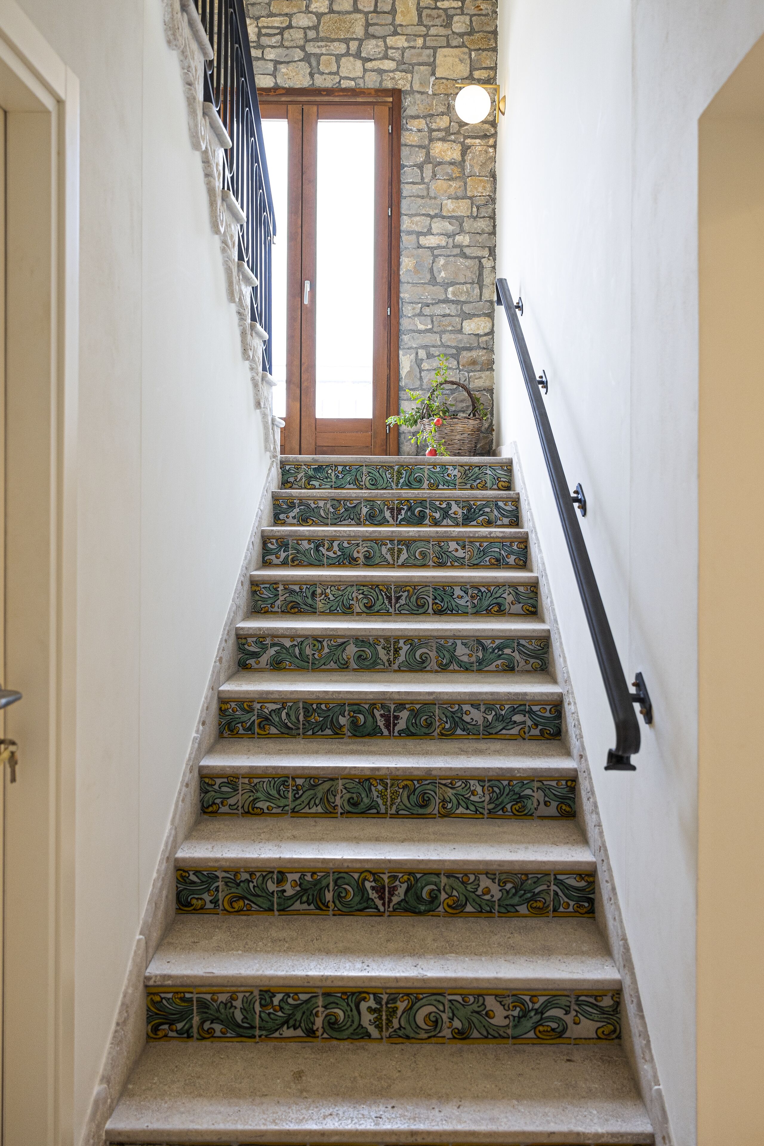 Un escalier orné de carreaux verts et jaunes, une porte en bois en haut, et un mur de pierre.