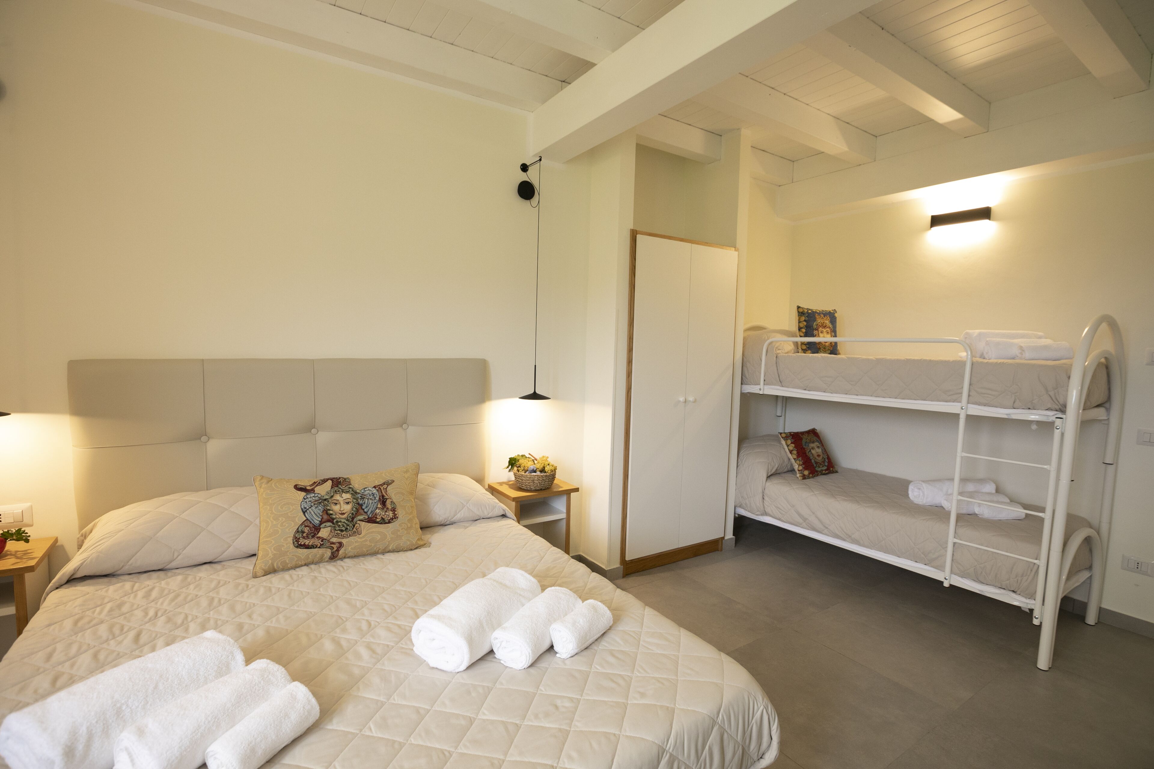 Une chambre avec un grand lit, un lit superposé plus petit et une table de chevet avec une lampe.