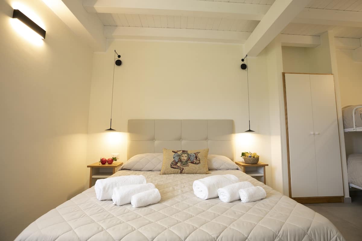 Una cama bien hecha con cabecera acolchada, dos mesitas de noche con lámparas y un armario.
