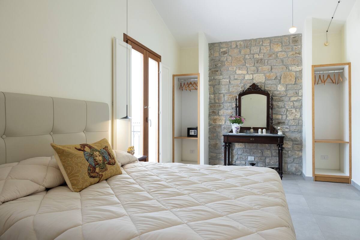 Un dormitorio con una cama grande, una pared de piedra, un aparador de madera y un espejo.