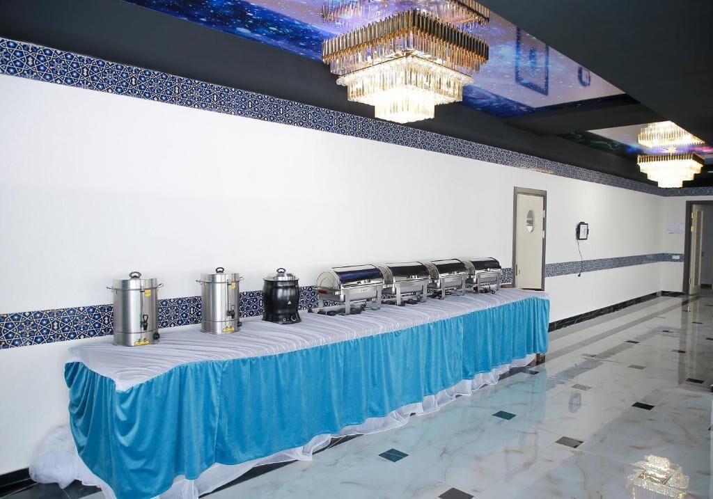 Una larga mesa de buffet con dispensadores de comida, un mantel azul y una araña.