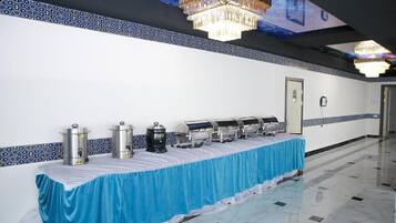 A long buffet table with food dispensers, a blue tablecloth, and a chandelier.