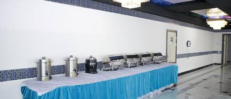 A long buffet table with food dispensers, a blue tablecloth, and a chandelier.
