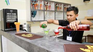 Um barista prepara uma bebida no balcão, com uma máquina de café e prateleiras cheias de bebidas ao fundo.