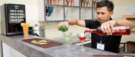 A barista preparing a drink at a counter with a coffee machine and shelves of beverages in the background.
