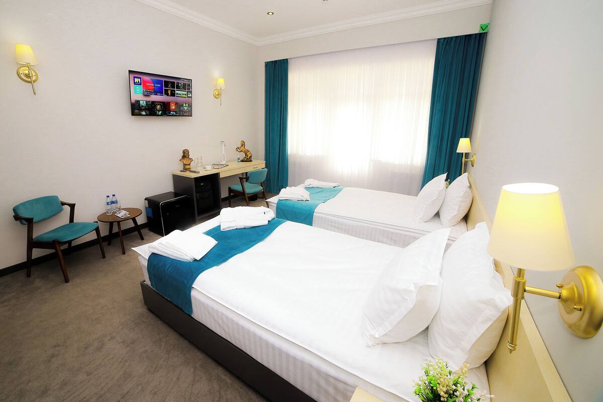 A hotel room with two beds, a desk, a chair, and a TV on the wall.