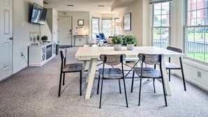A spacious dining area with a large table and chairs, a television mounted on the wall, and large windows providing natural light. - Historic Dtwn Home: 2 Mi to Military Park! (Gettysburg)