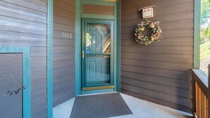Une maison en bois avec une porte verte, le numéro 1012, et une guirlande de fleurs accrochée au mur.
