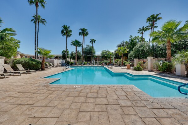 Relax by the serene pool surrounded by lush greenery and palm trees, with lounge chairs and a paved walkway.