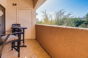 Un balcon avec une petite table et des chaises, une porte et une vue sur les arbres et les bâtiments.